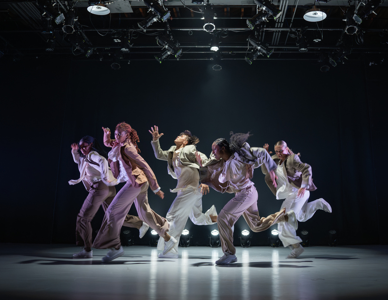 A group of AMDA Los Angeles dance students in baggy suits perform on a spotlit stage